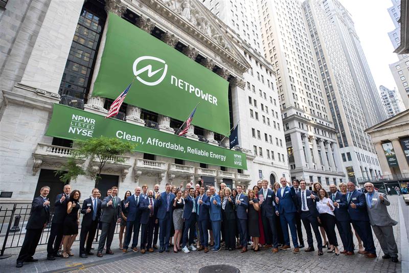 People posing in front of the New York Stock Exchange with "NETPOWER" banners displayed.