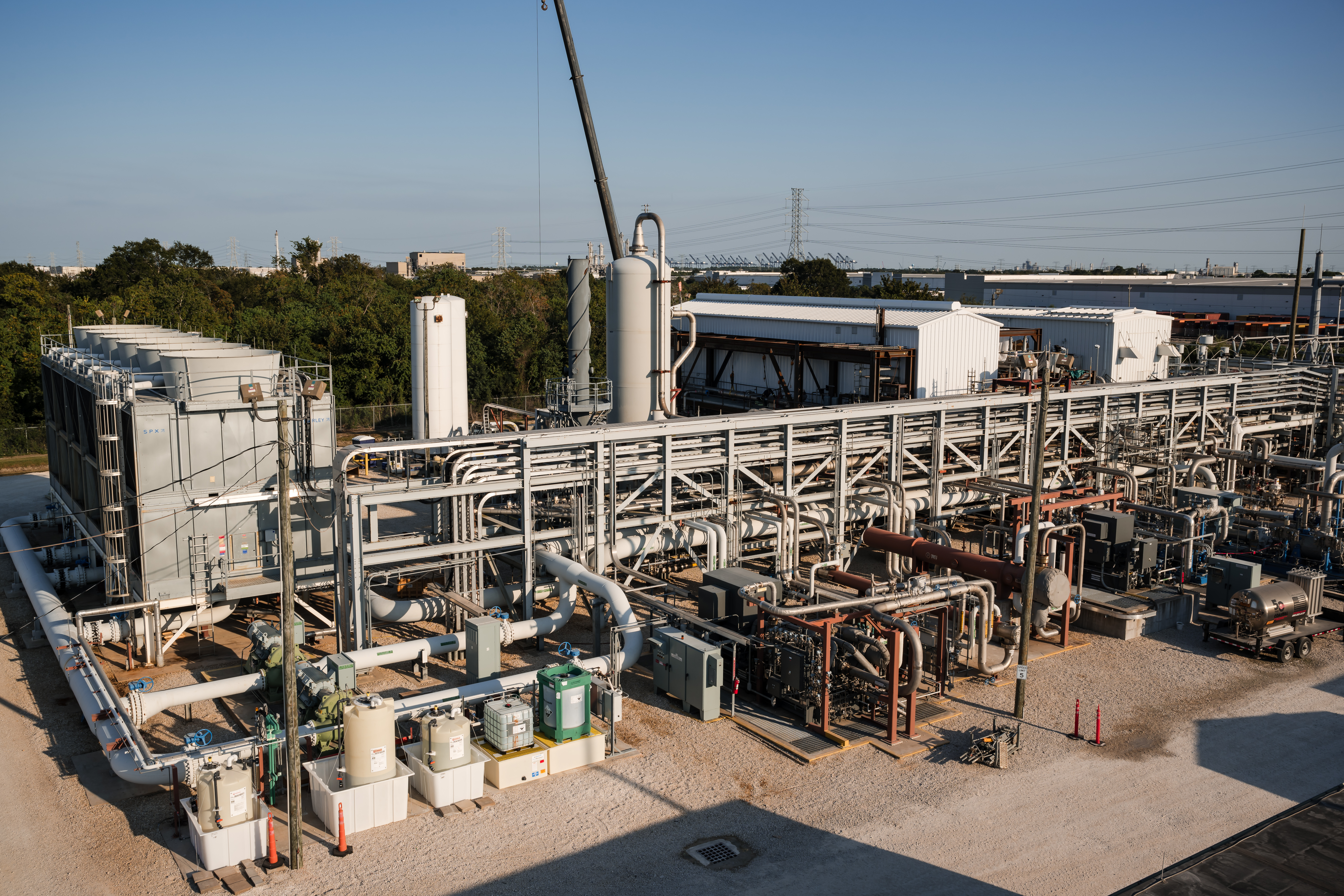 An industrial facility with a complex network of pipes, storage tanks, and machinery, set against a clear blue sky.