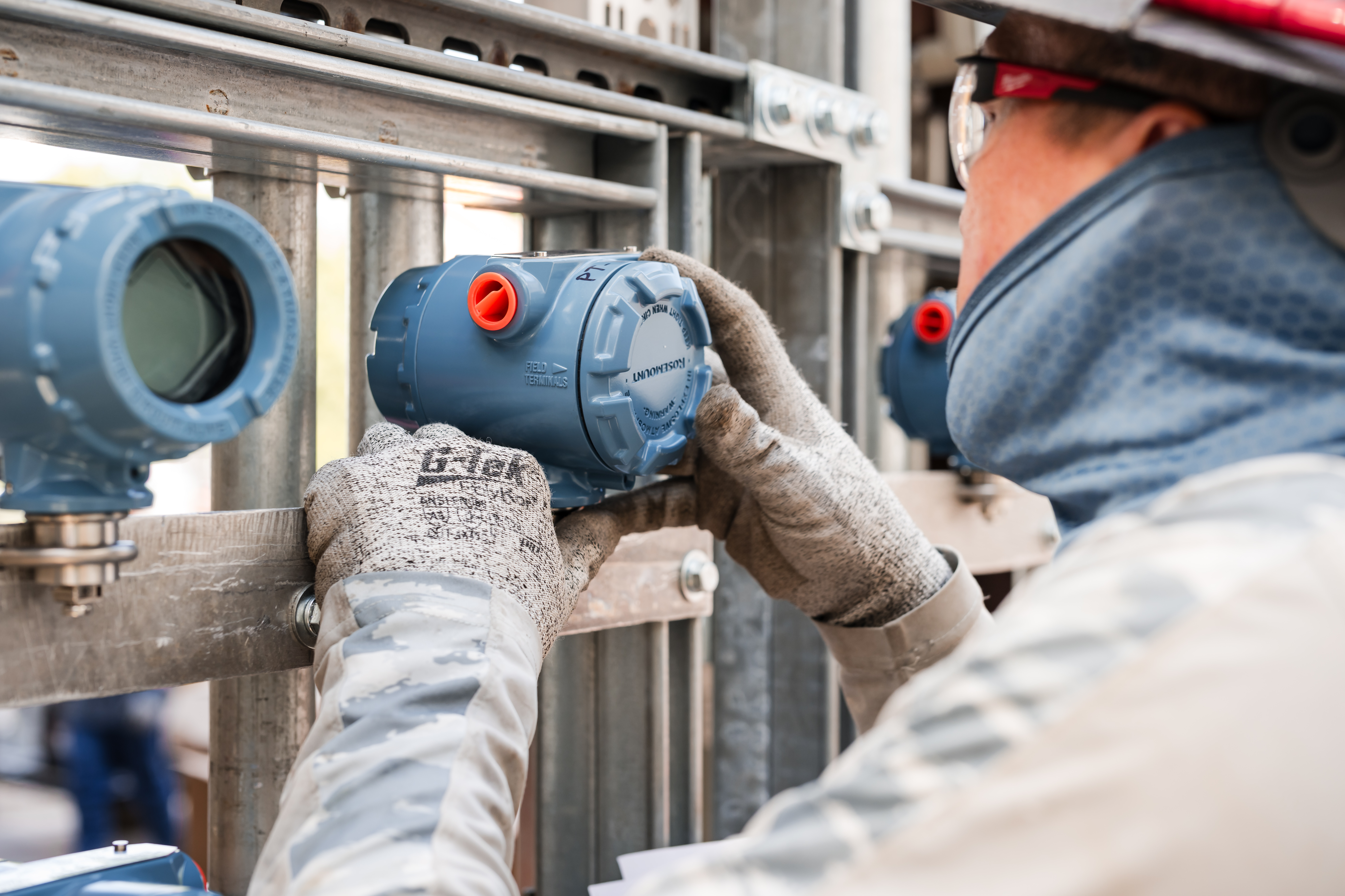 Person adjusting a blue industrial device on a metal framework.